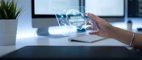 Woman's hand holding transparent digital globe with data network visualization on modern office desk with laptop and plant.