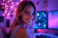 Young blonde woman smiling in neon lighting with purple and blue bokeh background, looking over shoulder in modern gaming setup environment with computer monitors.