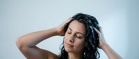 Young woman with wet dark hair applying hair treatment or shampoo in bathroom. Natural skincare and haircare routine for healthy lifestyle.