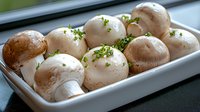 Fresh white button mushrooms garnished with chopped parsley in white ceramic dish, macro food photography showing texture and natural lighting.