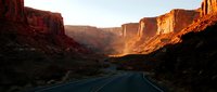 Desert highway winding through towering red rock canyon formations at golden hour sunset, scenic road trip travel destination.