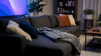 Cozy living room interior with gray upholstered sofa, decorative pillows, and knit throw blanket, illuminated by blue neon light for modern home decor and interior design projects.
