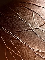 Close-up macro shot of brown leather texture with natural cracks and wrinkles creating abstract pattern. Dramatic lighting highlights surface details.