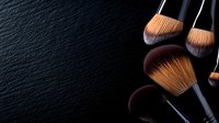 Professional makeup brushes with soft bristles arranged on dark textured background, dramatic side lighting creates artistic shadows and highlights cosmetic tools.