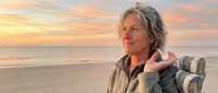 Senior man with long gray hair and light skin tone relaxing on beach chair at sunset, enjoying peaceful coastal scenery for lifestyle and wellness content.