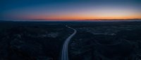 Aerial view of illuminated highway cutting through dark landscape at twilight with vibrant sunset sky, suitable for transportation, infrastructure, and travel concepts.