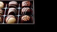 Luxury chocolate pralines with white and dark chocolate stripes in elegant black gift box against dark background, selective focus on gourmet confectionery assortment.