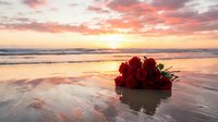 Red roses bouquet on sandy beach at sunset with golden sky and ocean waves reflecting romantic light for wedding anniversary celebration.