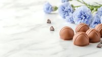 Milk chocolate truffles with blue carnation flowers on white marble background, selective focus. Sweet dessert composition for confectionery design.