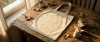 Natural linen tote bag on rustic wooden table with autumn leaves and warm sunlight streaming through window creating cozy seasonal atmosphere.