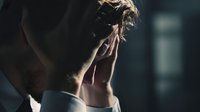 Stressed businessman holding head in hands showing mental exhaustion and workplace burnout in dark office environment for corporate wellness concepts.