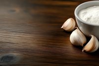 Fresh garlic cloves and white bowl with flour on rustic wooden table for cooking and baking preparation in kitchen.