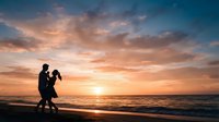 Silhouette of couple dancing on beach at sunset with golden sky and ocean waves, romantic evening scene for wedding and travel concepts.