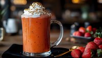Creamy strawberry smoothie with whipped cream topping in glass mug, fresh berries nearby on wooden table, warm cafe atmosphere for healthy drinks menu.