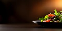 Fresh mixed salad with tomatoes and greens on black plate against dark background with copy space, dramatic food photography lighting.