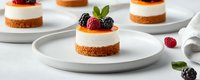 Mini no-bake cheesecakes topped with fresh blackberries, raspberries and mint leaves on white plates against light background, selective focus on dessert.