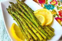 Fresh grilled asparagus spears garnished with bright lemon slices on white rectangular plate, vibrant green color and char marks visible, colorful table setting.