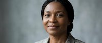 Professional African American businesswoman in elegant blazer smiling confidently against neutral background for corporate and leadership content.