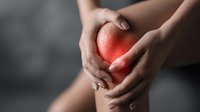 Female hands holding painful knee with red glow highlighting inflammation area, concept of joint pain, arthritis, and sports injury.