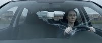 Young professional woman driving car in residential neighborhood during overcast day commuting to work or daily errands with focused expression.