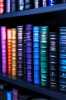 Colorful hardcover books arranged on wooden shelves in library, featuring vibrant spines in purple, blue, and teal tones with selective focus effect.