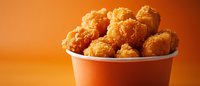 Crispy golden chicken nuggets in white container against vibrant orange background, appetizing fast food snack for menu advertising.