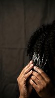 African American woman covering face with hands showing emotional distress or grief against dark background for mental health awareness campaigns.