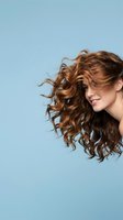 Young woman with flowing curly brown hair in motion against blue background for beauty and haircare advertising campaigns.