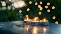 Glowing tea light candles on dark surface with bokeh lights in background creating cozy atmospheric mood. Romantic evening ambiance with soft candlelight.