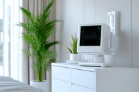 Modern hospital room with patient monitoring display screen on white cabinet, medical equipment and green palm plant near window, healthcare interior.