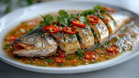 Steamed whole fish with soy sauce, chili peppers and fresh herbs on white plate. Traditional Asian cuisine dish with ginger and scallions for restaurant menu.
