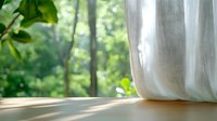 Sunlit window with flowing white curtain overlooking lush green forest, creating serene atmosphere for home interior design.