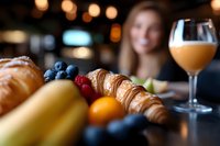 Fresh croissants with berries and orange juice create elegant breakfast scene while woman enjoys morning meal in cozy cafe with warm bokeh lighting atmosphere.