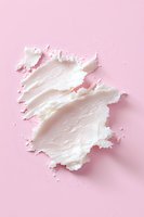 White creamy cosmetic texture smeared on pink background, moisturizer or face cream sample showing rich consistency and smooth application pattern.