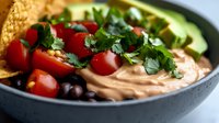 Healthy hummus bowl with cherry tomatoes, black beans, fresh herbs and avocado slices. Nutritious Mediterranean appetizer for clean eating lifestyle.