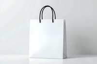 White paper shopping bag with black handles on light background, isolated mockup for branding and retail design presentation. Clean minimal style.