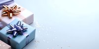 Elegant gift boxes in pastel pink and blue with metallic bows on light background with scattered sparkles, copy space for holiday greeting or celebration message.
