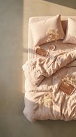 Cozy pink linen bedding with golden floral embroidery and natural sunlight creating warm shadows on unmade bed for home decor and lifestyle concepts.