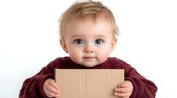 Caucasian baby in burgundy sweater holding cardboard, looking at camera with bright blue eyes and gentle smile against white background. For family, childhood concepts.