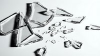 Shattered glass fragments scattered on white surface, broken pieces in various sizes creating abstract pattern for destruction, accident, or damage concepts.