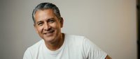Confident mature Hispanic man in white t-shirt smiling warmly at camera in soft natural lighting for lifestyle and wellness content.