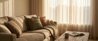 Cozy living room with beige upholstered sofa, decorative pillows, and sheer curtains filtering warm sunlight through windows for home decor and interior design projects.
