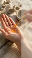 Woman applying golden facial serum oil drops from pipette dropper onto palm in natural sunlight with eucalyptus leaves for organic skincare routine.