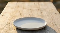 Empty white ceramic plate on rustic wooden table surface, suitable for food styling, restaurant menus, culinary blogs, and tableware product presentations.