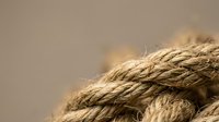 Close-up of natural jute rope with twisted fibers and warm lighting creating textured background for nautical and rustic design projects.