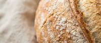 Freshly baked artisan bread loaf with golden crust and oats on rustic burlap background. Homemade bakery product for healthy eating and cooking concepts.