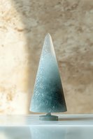 Minimalist frosted glass Christmas tree in teal ombre effect with snow-like texture, standing on reflective surface against neutral beige background.