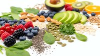 Colorful superfood ingredients including fresh berries, avocado slices, nuts, seeds and leafy greens arranged on white background for healthy nutrition concepts.