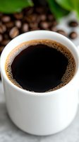 Fresh black coffee in white ceramic cup with foam bubbles and roasted beans in background, close-up view on marble surface for food and beverage marketing.