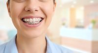 Young Asian woman with metal braces smiling showing orthodontic treatment in dental office for teeth straightening and oral health care.